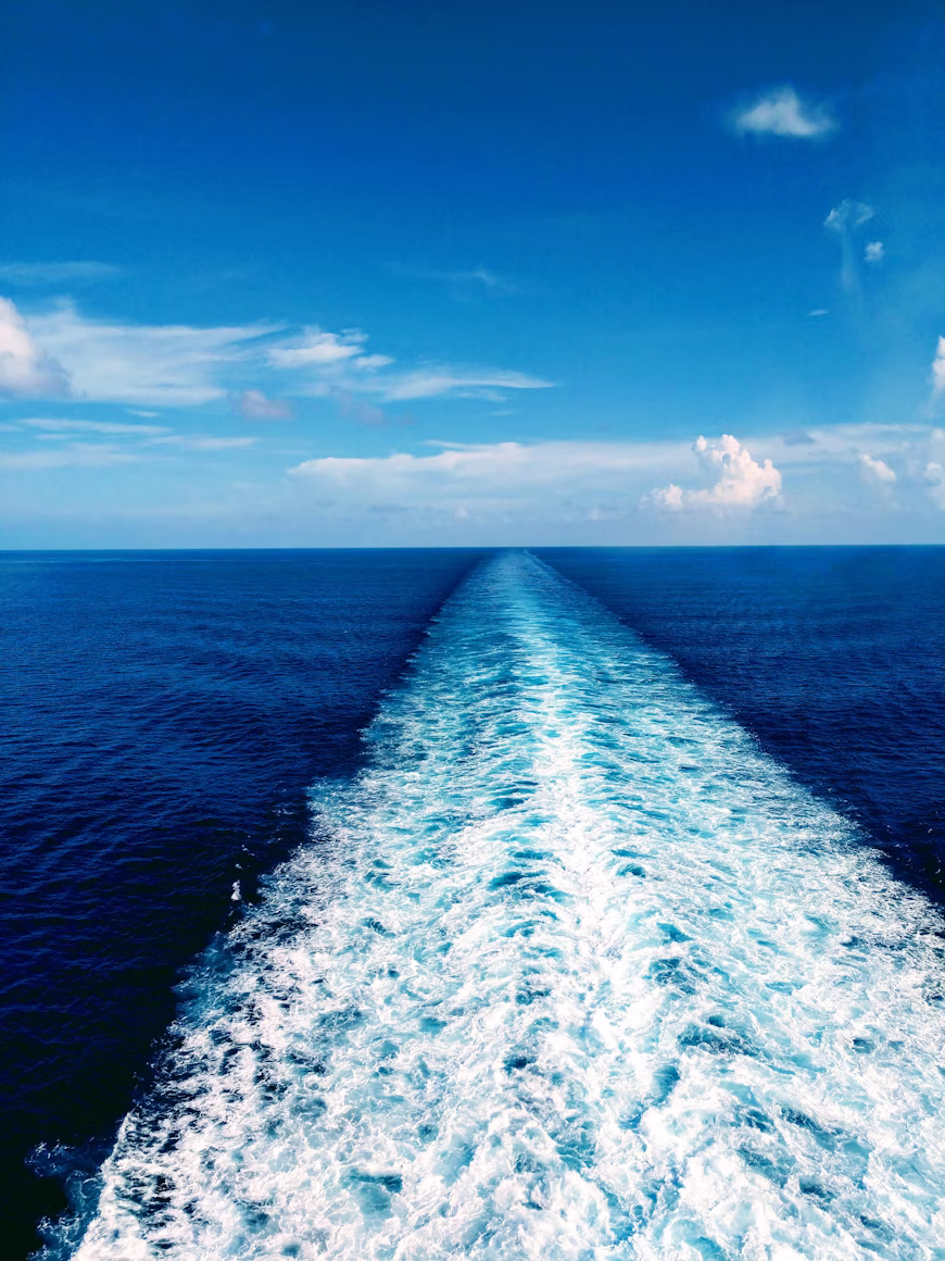 A long, luminous wave trail curling across dark water — the path of a vessel through the cycle.